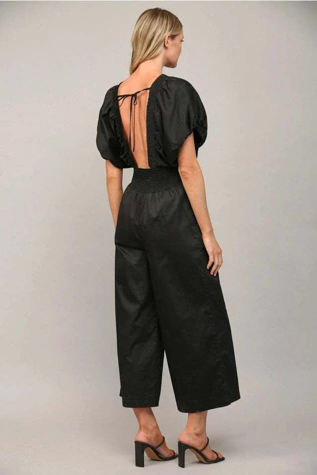 Woman wearing black open tie back jumpsuit with puff sleeves and wide legs.