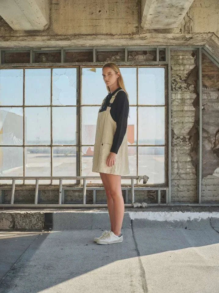 Corduroy overall mini dress with adjustable straps and button-down front, styled with a black long-sleeve top.