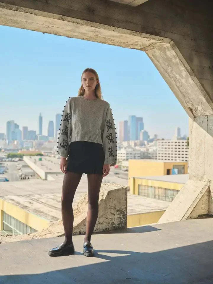 Sweater with embroidered sleeves and pom-pom details worn by model in urban setting.